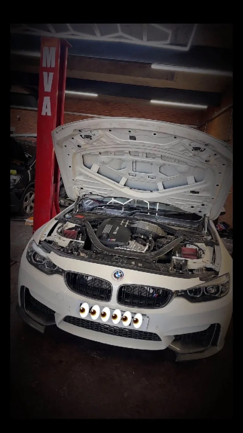 White BMW with its bonnet raised inside the workshop